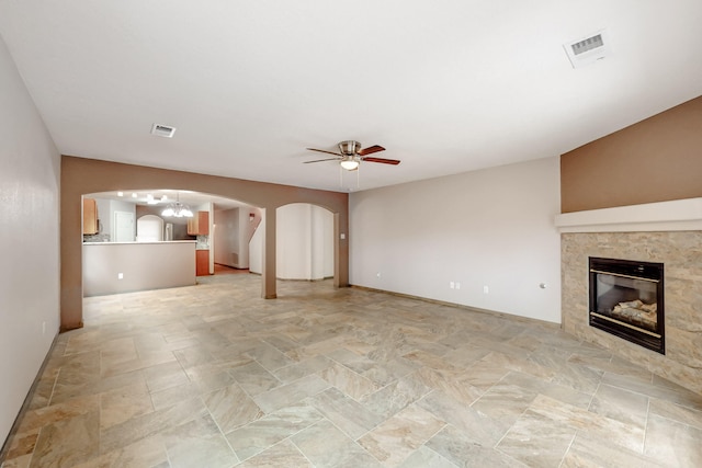 unfurnished living room featuring arched walkways, ceiling fan with notable chandelier, a tiled fireplace, and visible vents