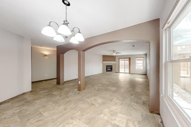 unfurnished living room featuring arched walkways, a glass covered fireplace, baseboards, and ceiling fan with notable chandelier