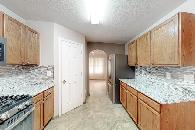 kitchen with arched walkways, appliances with stainless steel finishes, light stone counters, and tasteful backsplash