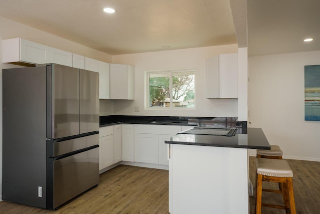 kitchen featuring a breakfast bar, freestanding refrigerator, white cabinets, and dark countertops