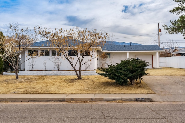 ranch-style home with fence, driveway, an attached garage, a shingled roof, and stucco siding