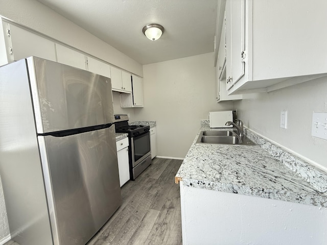 kitchen featuring light wood finished floors, light countertops, appliances with stainless steel finishes, white cabinetry, and a sink