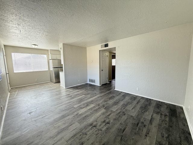 unfurnished bedroom featuring visible vents, a textured wall, wood finished floors, and freestanding refrigerator