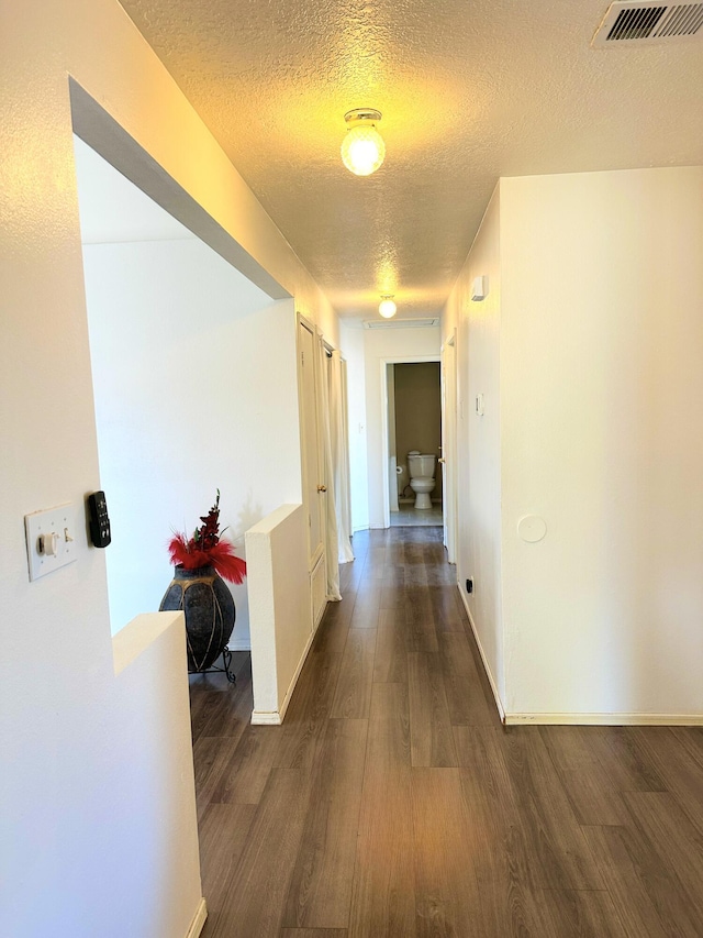 hallway with baseboards, a textured ceiling, visible vents, and dark wood-type flooring