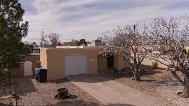 pueblo revival-style home featuring a garage, driveway, fence, and stucco siding