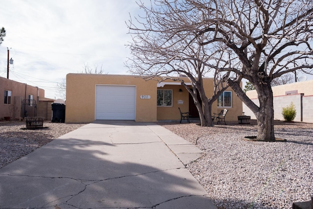 pueblo-style home with an attached garage, driveway, fence, and stucco siding