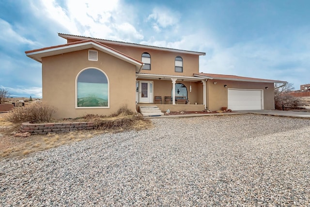 mediterranean / spanish home with an attached garage, stucco siding, a porch, and gravel driveway