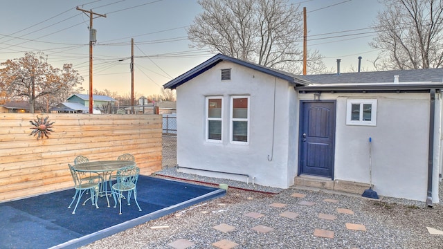 exterior space featuring a shingled roof, fence, and stucco siding