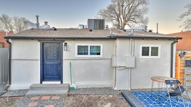 back of property at dusk featuring entry steps, central AC, and stucco siding