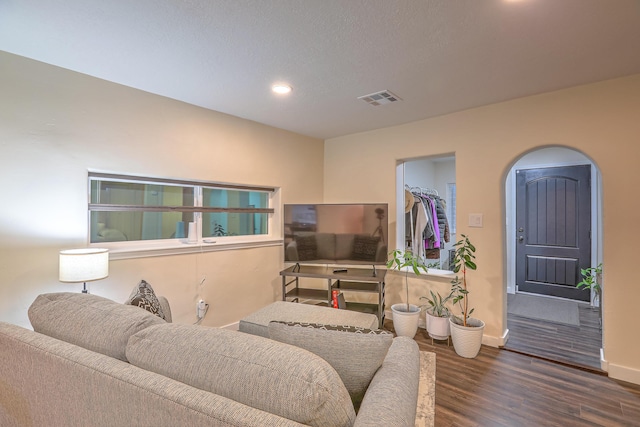 living room with arched walkways, dark wood-style flooring, recessed lighting, visible vents, and baseboards