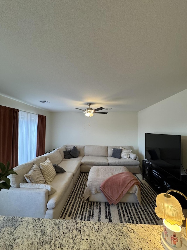 living room featuring visible vents, ceiling fan, and a textured ceiling