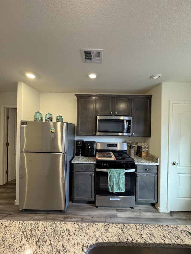 kitchen featuring dark brown cabinetry, visible vents, appliances with stainless steel finishes, a textured ceiling, and light wood-type flooring