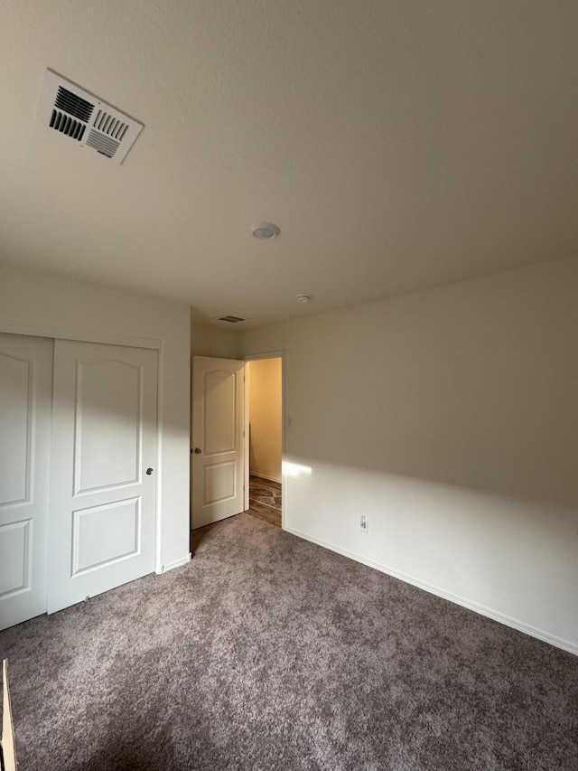 unfurnished bedroom featuring baseboards, visible vents, dark carpet, and a closet