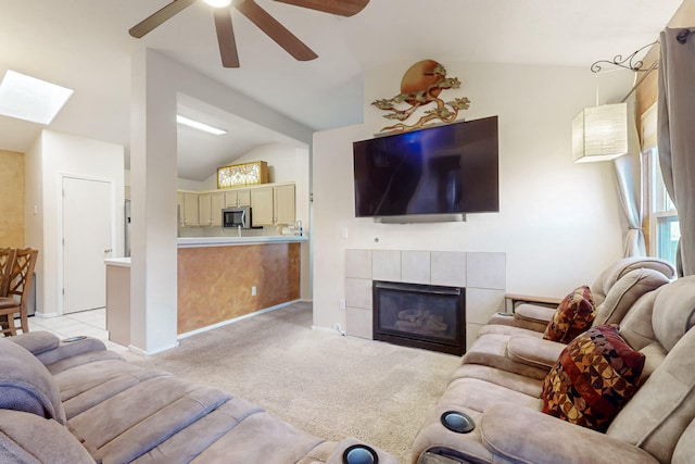 living area with vaulted ceiling with skylight, light carpet, a fireplace, a ceiling fan, and baseboards