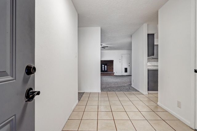 corridor with a textured ceiling, light tile patterned flooring, light carpet, and baseboards