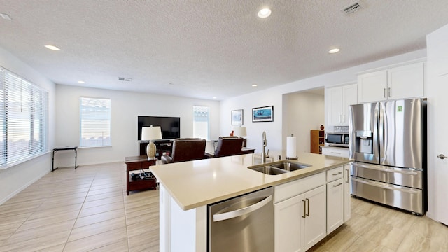 kitchen featuring appliances with stainless steel finishes, white cabinets, a sink, and a center island with sink