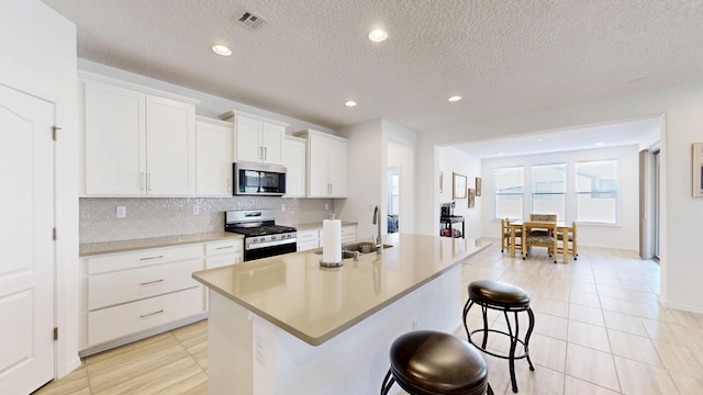 kitchen with appliances with stainless steel finishes, a kitchen island with sink, light countertops, and white cabinetry