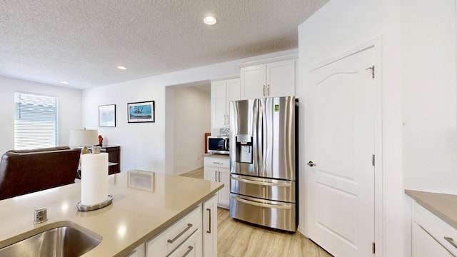 kitchen featuring stainless steel appliances, light countertops, light wood-style flooring, white cabinets, and a textured ceiling