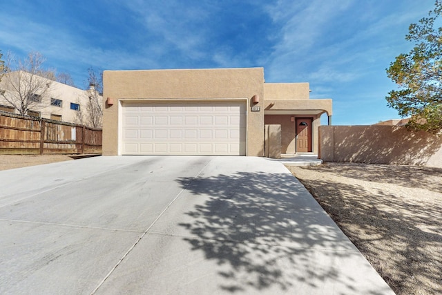 adobe home featuring a garage, concrete driveway, fence, and stucco siding