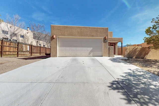 view of front of property featuring a garage, driveway, fence, and stucco siding