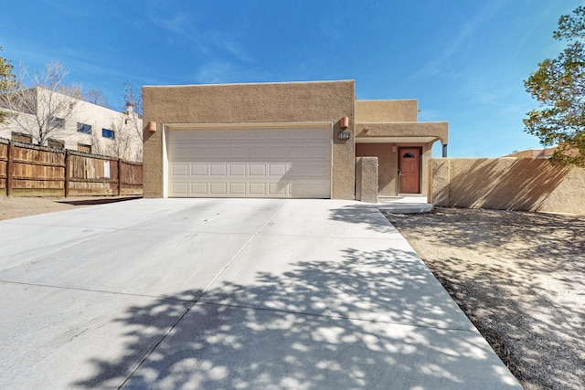 pueblo-style house featuring a garage, driveway, fence, and stucco siding