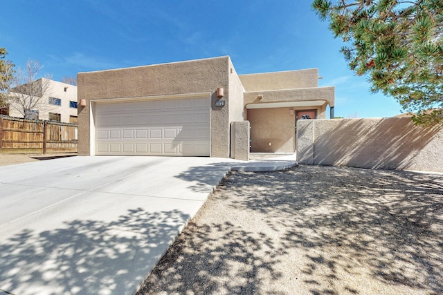 pueblo-style house featuring fence, driveway, an attached garage, and stucco siding