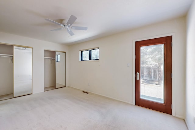 unfurnished bedroom with light carpet, visible vents, a ceiling fan, access to exterior, and multiple closets