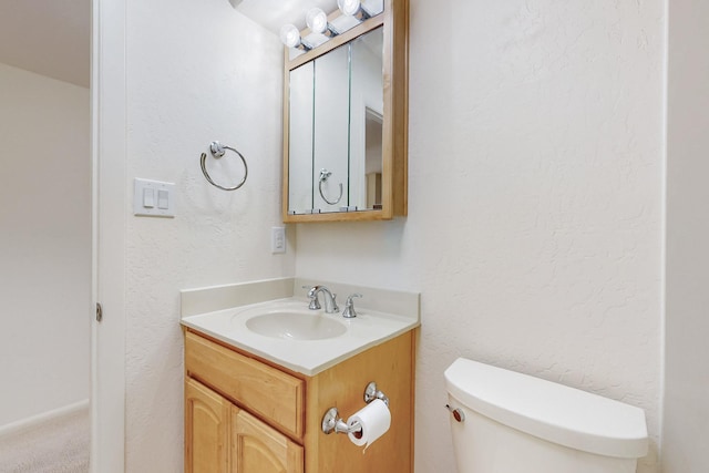 bathroom featuring a textured wall, vanity, and toilet