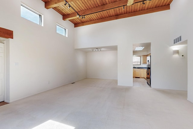 empty room with beam ceiling, rail lighting, visible vents, a towering ceiling, and wood ceiling