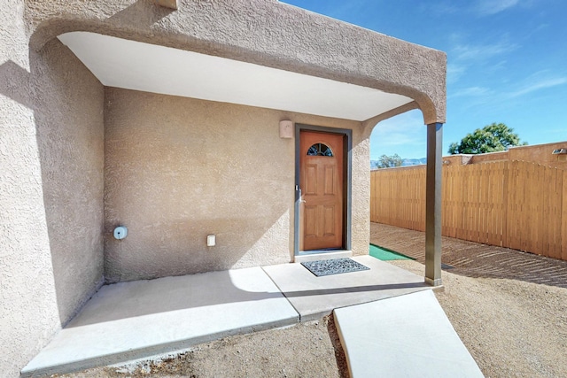 entrance to property featuring fence and stucco siding