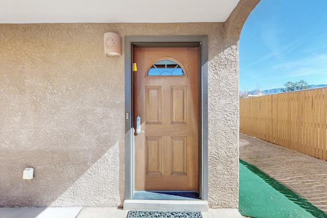 entrance to property featuring fence and stucco siding