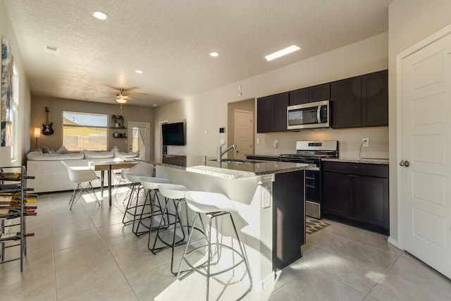 kitchen with stone countertops, stainless steel appliances, open floor plan, a kitchen bar, and a center island with sink