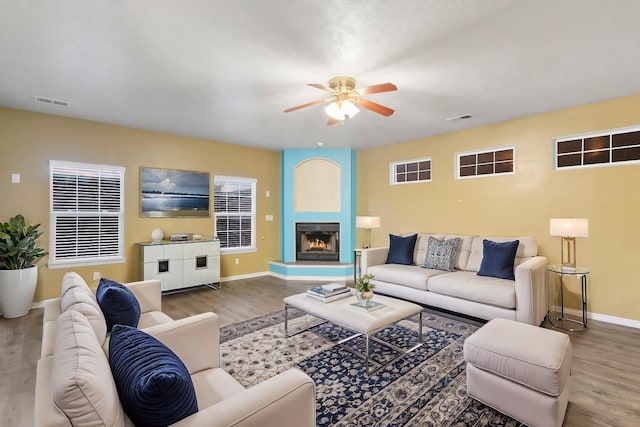 living room featuring a fireplace, wood finished floors, visible vents, and baseboards