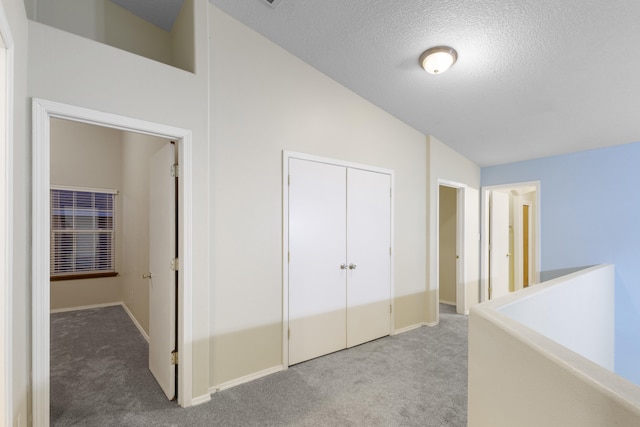 hallway with carpet, vaulted ceiling, a textured ceiling, and baseboards