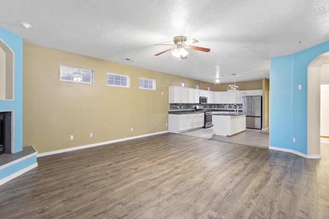 kitchen with arched walkways, white cabinets, a fireplace with raised hearth, appliances with stainless steel finishes, and open floor plan