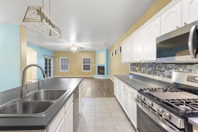 kitchen with white cabinets, a fireplace with raised hearth, open floor plan, stainless steel appliances, and a sink