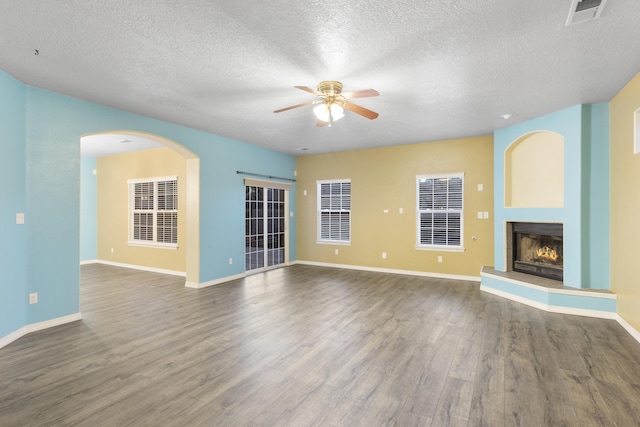 unfurnished living room featuring a lit fireplace, visible vents, ceiling fan, and wood finished floors