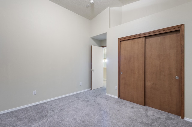 unfurnished bedroom with carpet floors, lofted ceiling, a closet, a textured ceiling, and baseboards