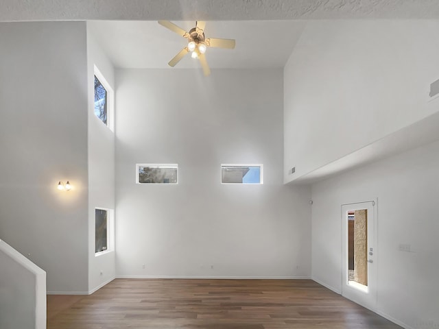 unfurnished living room featuring baseboards, wood finished floors, a towering ceiling, and a ceiling fan