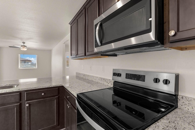 kitchen with a peninsula, dark brown cabinetry, appliances with stainless steel finishes, and light stone counters