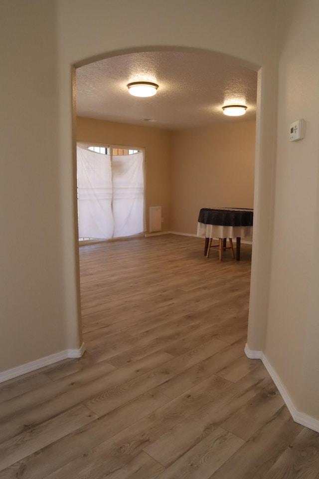 hall featuring arched walkways, a textured ceiling, baseboards, and wood finished floors