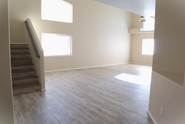 unfurnished living room with a towering ceiling, light wood finished floors, and stairs