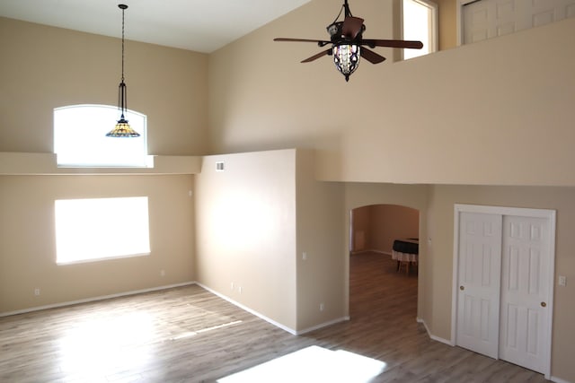 empty room with visible vents, arched walkways, a towering ceiling, ceiling fan, and wood finished floors