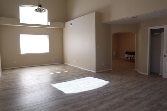 spare room featuring arched walkways, a healthy amount of sunlight, a towering ceiling, and wood finished floors