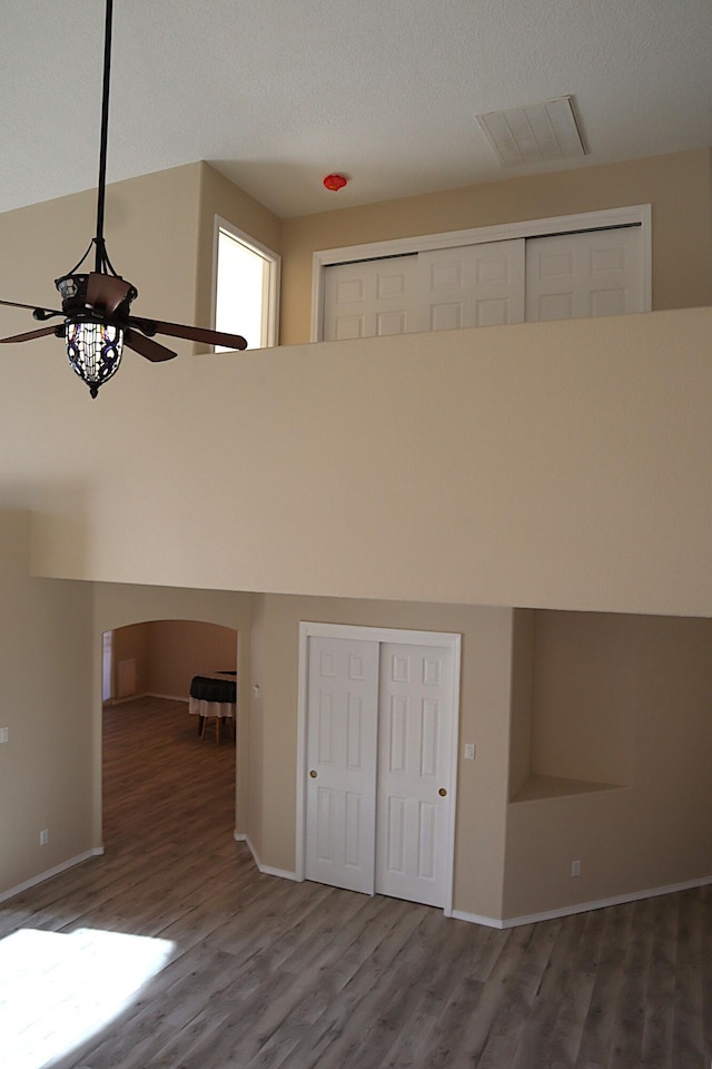 interior space featuring a towering ceiling, baseboards, visible vents, and wood finished floors