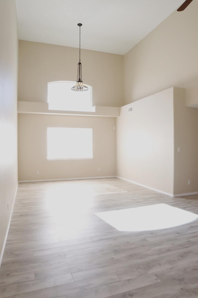 unfurnished room with light wood-type flooring, a towering ceiling, and baseboards