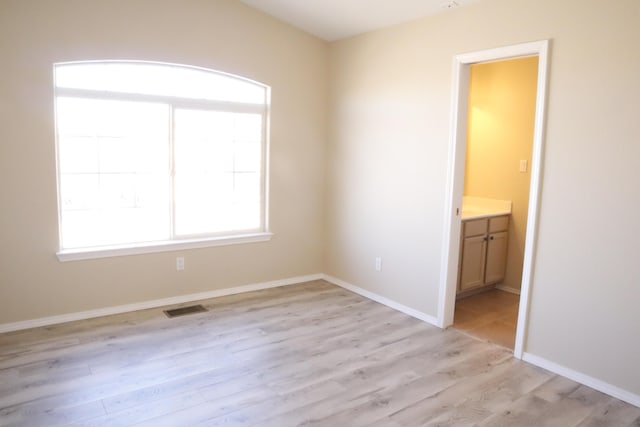 spare room with light wood-type flooring, visible vents, and baseboards