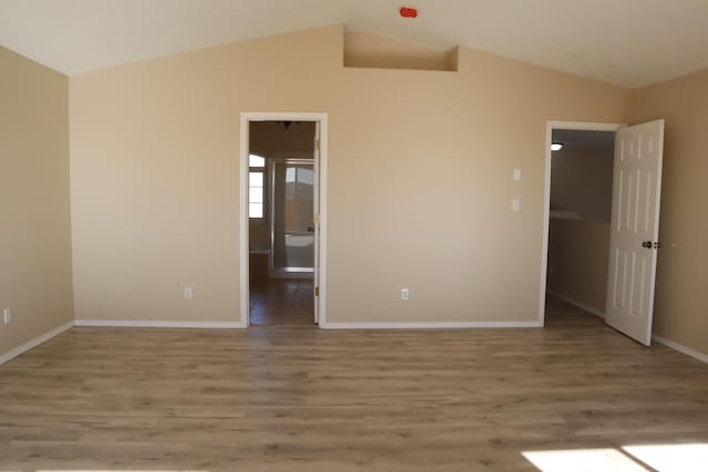 unfurnished bedroom featuring light wood-style flooring, baseboards, and vaulted ceiling