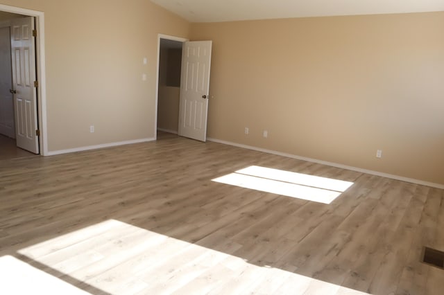 empty room featuring baseboards, lofted ceiling, visible vents, and light wood-style floors