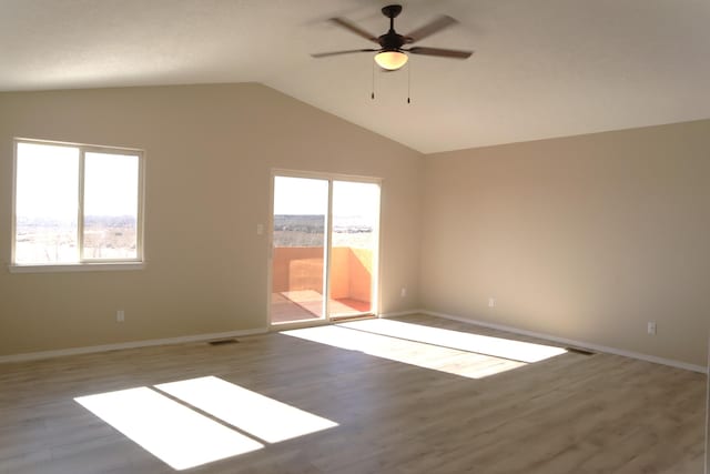 empty room with visible vents, ceiling fan, vaulted ceiling, wood finished floors, and baseboards